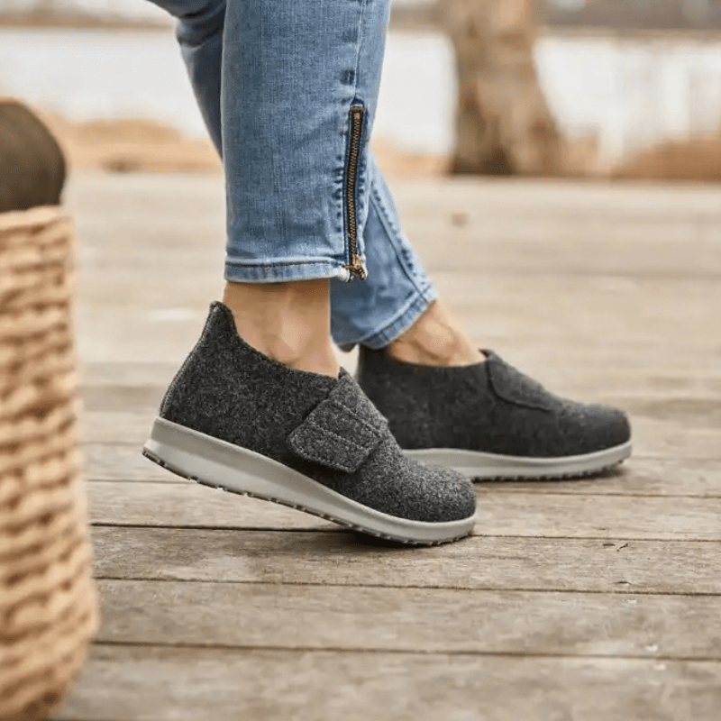 Femme portant des chaussons New Feet gris anthracite sur un parquet, vue latérale des pieds