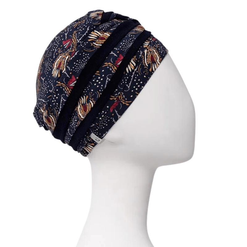 Turban Shanti imprimé Amber Garden vu de côté droit sur mannequin, avec couleurs bleu foncé et motif de plumes et de tiges