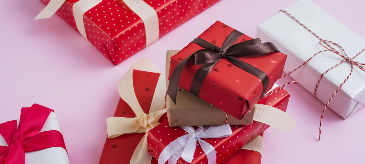 Plusieurs cadeaux emballés en rouge, blanc et marron avec des rubans et de la ficelle sur fond rose