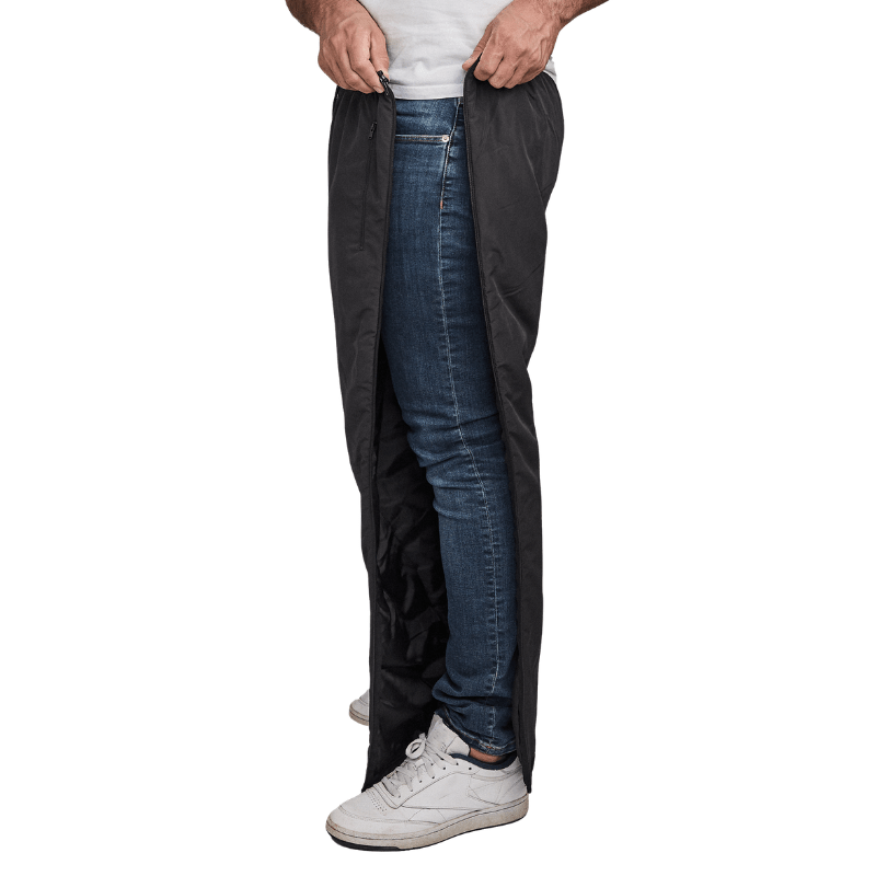 Homme ouvrant un pantalon thermique Dobsom noir sur le côté, par-dessus un jean bleu et des baskets blanches