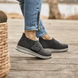Femme portant des chaussons New Feet gris anthracite sur un parquet, vue latérale des pieds