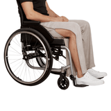 Une personne en fauteuil roulant portant un pantalon de jogging gris avec une fermeture éclair latérale ouverte montrant la jambe