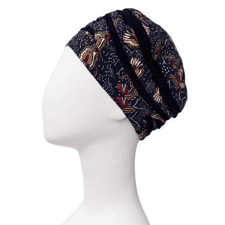 Turban Shanti imprimé Amber Garden vu de côté sur un mannequin blanc, avec base bleu foncé et motif de plumes et de tiges